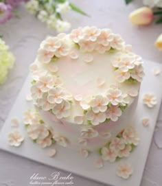 a white cake with flowers on it sitting on top of a table next to flowers