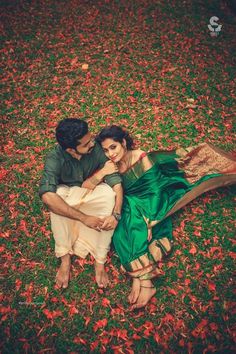 a man and woman laying on the ground in front of leaves with their arms around each other