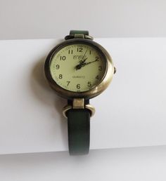 This is a women's watch with a green (made in Germany) leather flat cord strap. The style is retro minimalist with a simple distress look. The face of the watch is made in aged bronze finished alloy, free of nickel and lead, round shape 1.25 inches diameter. The strap comes in 6 sizes: XS for a 6.00 inches wrist S for a 6.25 inches wrist M for a 6.50 inches wrist L for a 6.75 inches wrist XL for a 7.00 inches wrist XXL for a 7.25 inches wrist If you need another size, please send me a message. T Classy Watch, Watch Women's, Retro Minimalist, Watches Women Leather, Minimalist Watch, Aged Bronze, Watch Battery, Watch For Women, Simple Leather