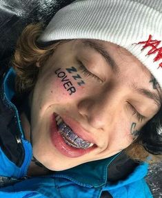 a young boy with his face painted red and black, smiling at the camera while wearing a white beanie