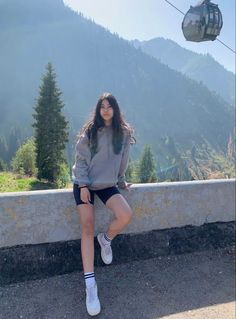 a woman sitting on the side of a road next to a cable car with mountains in the background