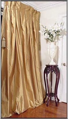 a white vase with flowers sitting on top of a wooden table next to a curtain