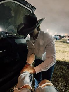 a man in a cowboy hat touches the hood of a car with his hand on another person's leg