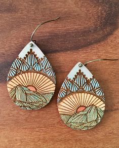 two wooden earrings with designs on them sitting on top of a wooden table next to a pair of scissors