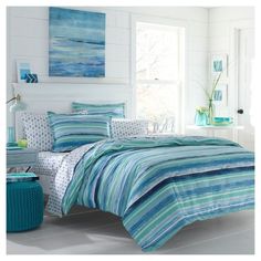 a bed with blue and green striped comforters in a white room next to a window