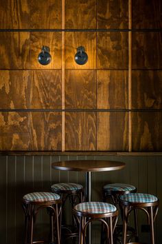 three stools and a table in front of a wooden wall with lights on it