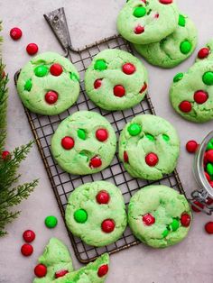 green cookies with red and green candies on a cooling rack next to christmas decorations