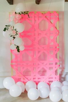 balloons and flowers are on the floor next to a pink wall with white balls hanging from it