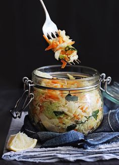 a fork full of coleslaw being lifted out of a glass jar with shredded cabbage and carrots