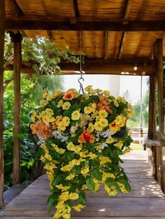 a hanging basket filled with yellow and red flowers on a wooden porch next to trees