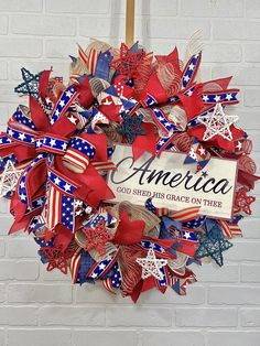 a patriotic wreath with red, white and blue ribbons hanging on a brick wall next to a sign that says america