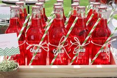 red soda bottles with green and white striped straws in a wooden crate at an outdoor party