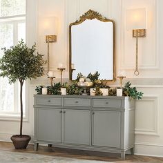 a table with candles, potted plants and a large mirror on the wall above it