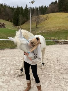 a woman is holding the head of a white horse while standing in an open area