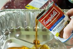 a person pouring mustard into a pan with meat in the back ground and seasoning on top