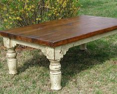 an old wooden table sitting in the grass next to a bush with yellow flowers on it