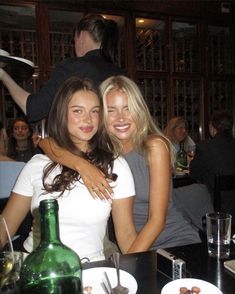 two beautiful young women sitting next to each other in front of a table with food and drinks