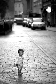 a small child is standing on a brick road in the middle of an alleyway