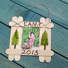 an ornament hanging on a wooden fence with a photo and trees in the frame