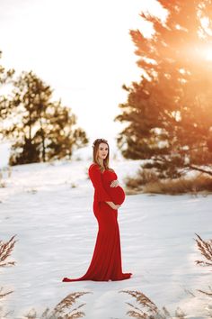 a pregnant woman in a red gown stands in the snow with her hands on her stomach