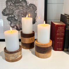 three white candles sitting on top of a table next to books and a framed photograph