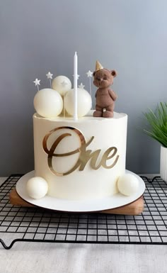 a birthday cake with a teddy bear on top and one candle in the middle that says one