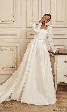 a woman in a long white dress standing next to a table with a drawer on it