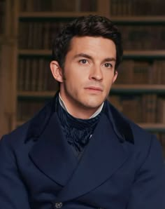 a man in a blue coat is posing for a photo with bookshelves behind him