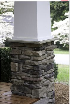 a wooden bench sitting next to a tall white pillar on top of a stone wall