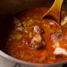 a pot filled with meat and vegetables being stirred by a wooden spoon