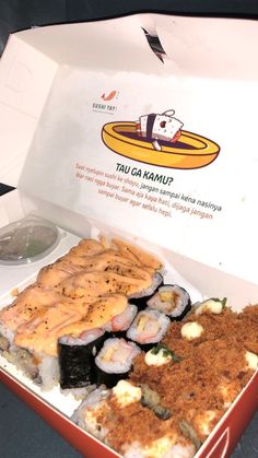 an open box filled with different types of sushi and other food on top of a table