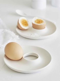 two plates with eggs on them sitting on a white counter top next to a cup and spoon