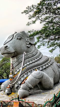 a statue of a bull with chains on it's neck and legs, sitting in front of trees