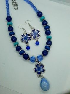 This beautiful set features blue and white flowers in the earrings and the main pendant of the necklace.  The necklace features different shades of blue beads to compliment the pendant. This is a great statement piece to set off any outfit and a must-have for women who want a unique necklace to show their personal style. Depending on the size, all jewelry comes shipped in either a box with cotton padding or wrapped carefully in tissue paper and mailed in a thick padded envelope to ensure it reac Blue Beaded Round Beads Jewelry Sets, Blue Beaded Jewelry Sets With Round Beads, Blue Beaded Jewelry Sets, Blue Beaded Flower Jewelry, Blue Flower-shaped Beaded Jewelry, Bohemian Blue Flower Necklace, Blue Beaded Jewelry Sets For Gift, Blue Jewelry Sets With Round Beads As A Gift, Handmade Blue Dangle Jewelry Sets