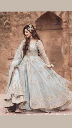 a woman in a blue and white gown standing on a stone floor with flowers around her