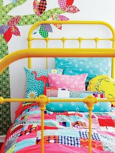 a yellow bed topped with lots of pillows next to a wall mounted bird decal