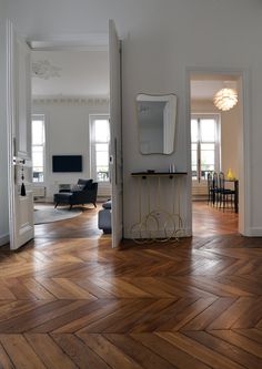 an open door leading to a living room with wood floors and white walls, along with a mirror on the wall