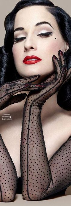 a woman with long black hair and red lips wearing fishnet stockings, holding her hands to her face