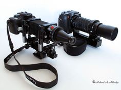 two cameras sitting next to each other on top of a white table with a black strap