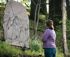 a woman standing next to a large rock in the middle of a forest with graffiti on it