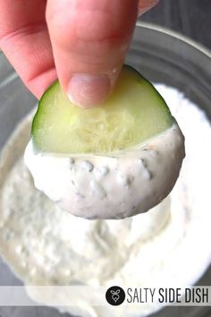 a hand dipping a cucumber into a bowl of dip