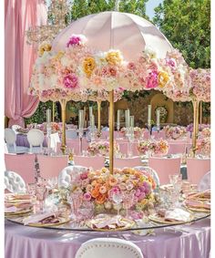 a table set up for a wedding with pink and yellow flowers on it, under an umbrella