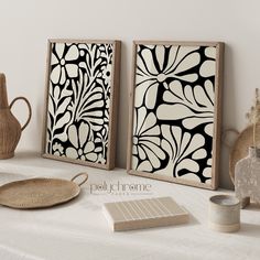 two black and white paintings sitting on top of a table next to a vase with flowers