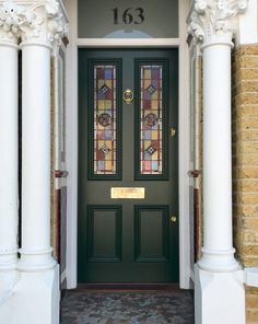 a green front door with stained glass on the top and bottom panel is flanked by two white pillars