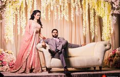 a man and woman sitting on a couch in front of a flower covered stage with flowers hanging from the ceiling