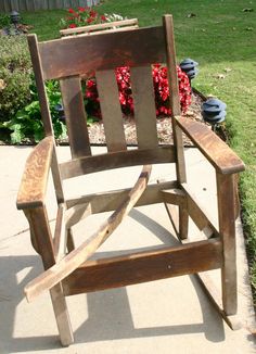 a wooden rocking chair sitting on top of a cement ground next to a flower garden