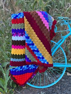 a colorful crocheted blanket sitting on top of a blue bike wheel in the grass