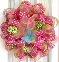 a pink and green mesh wreath with polka dots on the front door, decorated with flowers