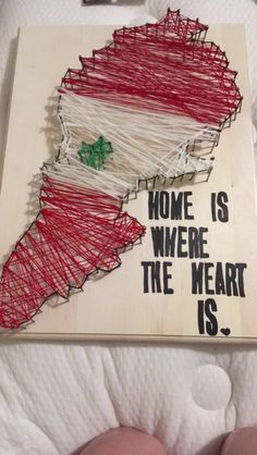 a wooden sign that says home is where the heart is with string wrapped in red, white and green