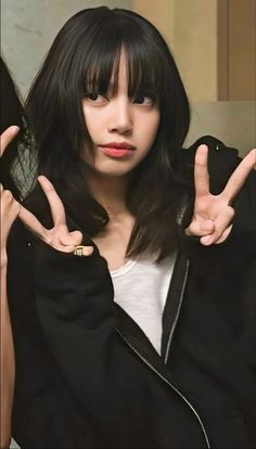 a woman with long black hair and bangs making the peace sign in front of her face